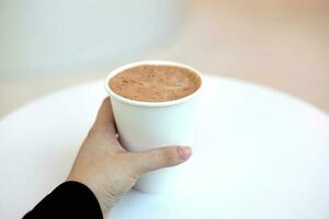 cacao melk papier kop Holding in vrouw hand- met wit tafel in cafe foto