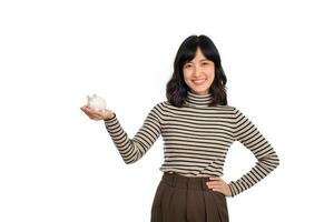 portret van jong Aziatisch vrouw gewoontjes uniform Holding wit varkentje bank geïsoleerd Aan wit achtergrond, financieel en bank besparing geld concept foto