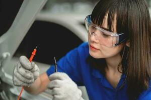 een deskundige vrouw monteur en controleren de auto accu met een jumper kabel in de motor kamer. reparatie onderhoud concept auto monteur in onderhoud centrum foto