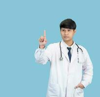 Aziatisch Mens leerling wetenschapper of dokter een persoon, vervelend een wit gewaad, staan, op zoek en lachend, blauw achtergrond met een stethoscoop ausculteren de hart in de omgeving van zijn nek. foto