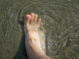 voet ondergedompeld in verkoudheid zee water Aan de strand gedurende de vakantie foto