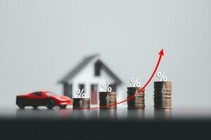 stapels van munten en model- huis en auto met percentage symbool voor toenemend interesseren tarieven. interesseren tarief financieel en hypotheek tarieven. icoon percentage symbool en pijl richten omhoog. foto