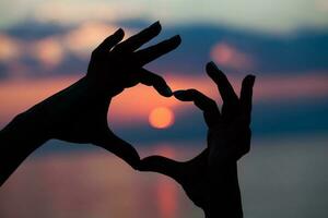 handen met hart vorm over- de zonsondergang foto