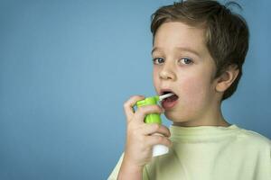 een schattig Kaukasisch jongen in een geel t-shirt sprays een aërosol in zijn mond naar traktatie een zeer keel foto