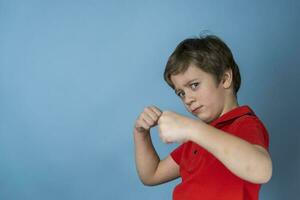 een schattig Kaukasisch jongen van 5 jaren oud in een rood t-shirt uitgerekt uit zijn handen met vuisten en staat in een boksen houding foto