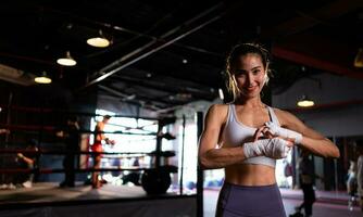 portret van vrouw aan het leren Muay Thais naar bouwen omhoog de sterkte van de lichaam en gebruik het voor zelfverdediging. zijn gebruik makend van hand- wraps voordat zetten Aan boksen handschoenen voor boksen foto