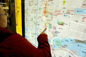 osaka, Japan, mei 19, 2018 - Chinese vrouw toerist op zoek Bij en vind attracties van Osaka stad in een stad kaart Bij de osaka's metro stad kaart bord. foto