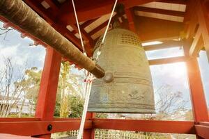 groot messing boeddhistisch klok en klop klok hout van Japans tempel in rood paviljoen Aan helder blauw lucht met zon en lens gloed achtergrond. foto