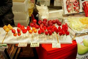 aardbei en kers in houten stokjes met Japans naam en prijs etiketten. uitverkoop Bij kuromon straat markt, osaka, Japan. foto