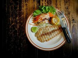 dolly vis steak bord, mes, en vork voor gemengd salade Aan een houten tafel foto