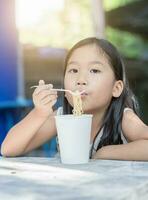 schattig Aziatisch kind meisje aan het eten instaan noodle beker, foto