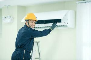 een Aziatisch jong technicus onderhoud Mens vervelend blauw uniform controleren, professioneel lucht conditioner installateur onderhouden modern binnen- lucht conditioner ruimte voor tekst foto