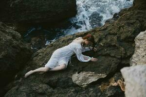 vrouw aan het liegen Aan haar terug Aan een rotsachtig kust visie van bovenstaand foto