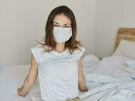 een vrouw in een medisch masker in een t-shirt en shorts zit Aan de bed foto