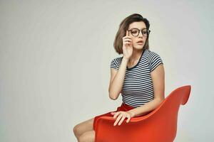 mooi vrouw in modieus kleren zittend Aan de rood stoel foto