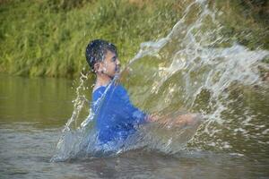 Aziatisch jongen in blauw t-shirt is uitgeven zijn vrije tijd door duiken, zwemmen, het werpen rotsen en vangen vis in de rivier- gelukkig, hobby en geluk van kinderen concept, in beweging. foto