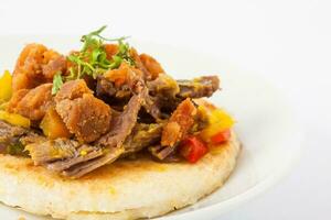 Colombiaanse arepa bekroond met versnipperd rundvlees en varkensvlees korst foto