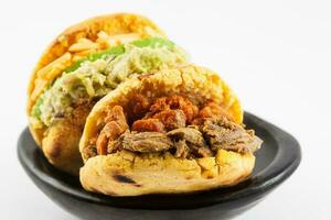 arepas met twee verschillend vullingen geserveerd in een zwart keramisch schotel Aan wit achtergrond foto