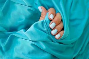 vrouw handen met een mooi manicure Aan een blauw achtergrond. zomer tendens, blauw helling Aan de nagels met gel Pools, schellak. kort nagels foto