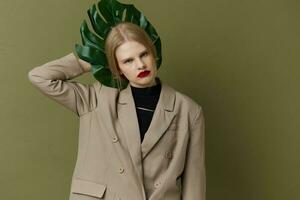 blond vrouw in jas rood lippen mode palm blad groen achtergrond foto
