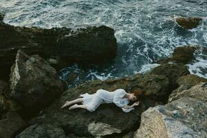 mooi vrouw aan het liegen Aan rotsachtig kust met scheuren Aan rotsachtig oppervlakte vakantie concept foto