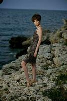 mooi vrouw staand Aan stenen poseren in strand jurk elegantie foto