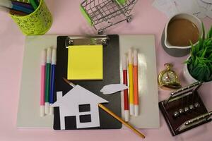 top visie van de snijdend papier of tekening huis Aan een roze tafel, voorbereidingen treffen naar Doen huiswerk in een klembord. tekening werken bureau concept foto