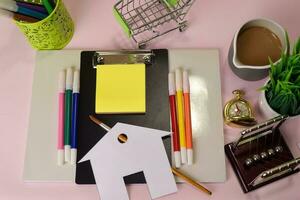 top visie van de snijdend papier of tekening huis Aan een roze tafel, voorbereidingen treffen naar Doen huiswerk in een klembord. tekening werken bureau concept foto