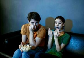 emotioneel vrouw en Mens met een bord van popcorn aan het kijken TV in de avond binnenshuis foto