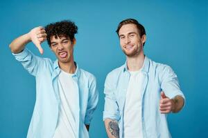 twee vrienden in identiek overhemden en een t-shirt gebaren met hun handen Aan een blauw achtergrond foto