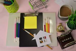 top visie van de snijdend papier of tekening huis Aan een roze tafel, voorbereidingen treffen naar Doen huiswerk in een klembord. tekening werken bureau concept foto