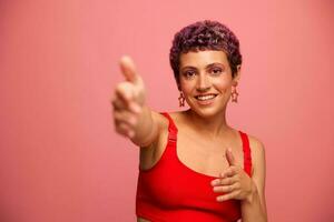 mode portret van een vrouw met een kort kapsel van Purper kleur en een glimlach met tanden in een rood top Aan een roze achtergrond dansen gelukkig foto