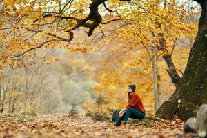 vrouw met rugzak in herfst Woud zittend in de buurt boom landschap vers lucht park foto