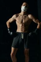 sportief Mens in medisch masker en in boksen handschoenen Aan zwart achtergrond shorts geschiktheid foto