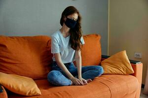 portret van een vrouw vervelend een masker zit Aan een oranje sofa Bij huis levensstijl foto