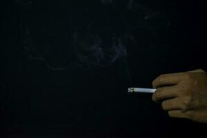 hand- van Aziatisch Mens Holding sigaretten met zwart achtergrond. roken sigaretten concept foto
