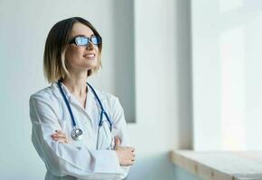 professioneel dokter vrouw met bril in de buurt venster en stethoscoop foto