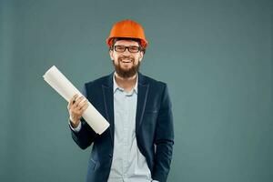 een Mens in een pak in een oranje moeilijk hoed blauwdrukken in de handen van een bouw ingenieur foto