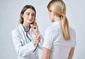 dokter in een medisch japon Aan een licht achtergrond en een blond vrouw geduldig foto