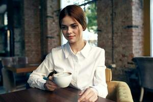 schattig bedrijf vrouw zittend in een cafe Bij de tafel een kop van drinken levensstijl foto