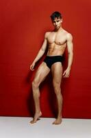 naakt mannetje bodybuilder in zwart slipje Aan een rood achtergrond en vol lengte foto