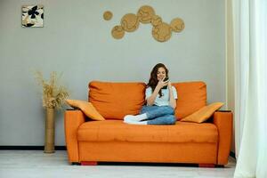 mooi vrouw chatten Aan de oranje bankstel met een smartphone appartementen foto