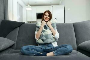 vrolijk vrouw met een hoofdkussen in haar handen zit Aan de sofa rust uit appartement interieur foto