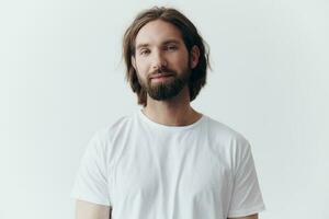 portret van een vrolijk Mens met een zwart dik baard en lang haar- met een soort glimlach in een wit t-shirt Aan een wit geïsoleerd achtergrond foto