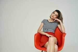 mooi vrouw in modieus kleren zittend Aan de rood stoel poseren studio foto