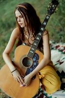 een meisje in eco-kleding hippie zittend met een gitaar en op zoek Bij een zonsondergang in de zomer foto