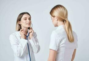 dokter in een medisch japon Aan een licht achtergrond en een blond vrouw geduldig foto