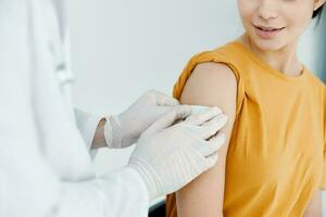 dokter in beschermend handschoenen banden de schouder van een vrouw in een geel t-shirt covid vaccinatie foto