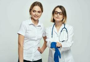 vrouw dokter in een medisch japon en in blauw handschoenen met een stethoscoop in de omgeving van haar nek en een vrouw geduldig foto