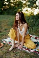 jong mooi hippie vrouw zittend Aan de grond in natuur in de herfst in eco kleding in de zonsondergang licht, een levensstijl van reizen en harmonie met de wereld foto